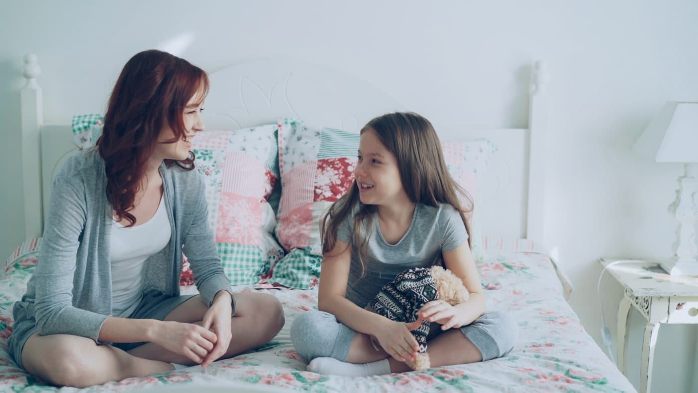 Een moeder en haar dochter zitten samen op bed te praten.